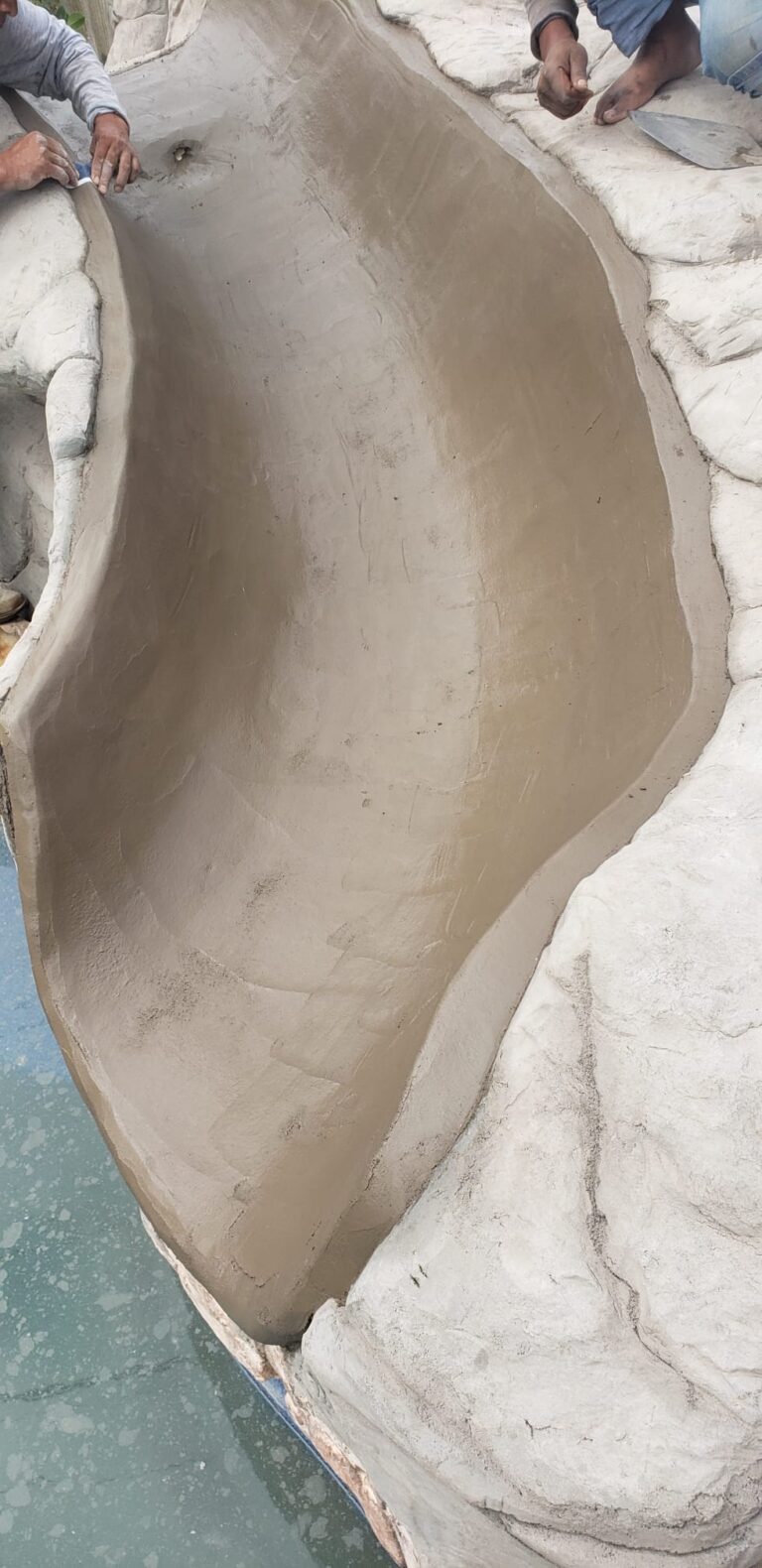 Craftsmen hand-shaping the concrete channel of a custom rock pool slide