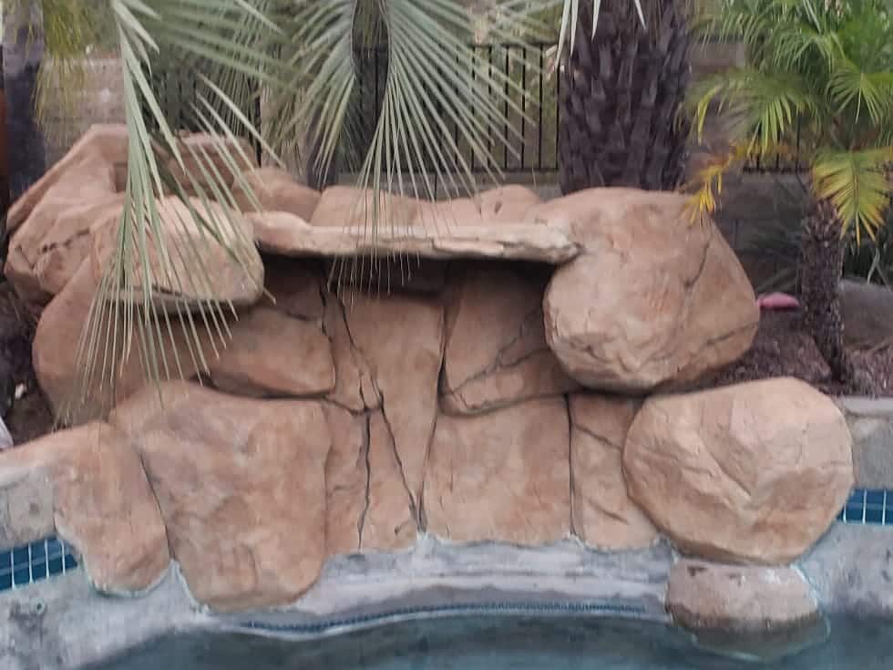 Artificial rock grotto water feature beneath palm trees at the edge of a spa