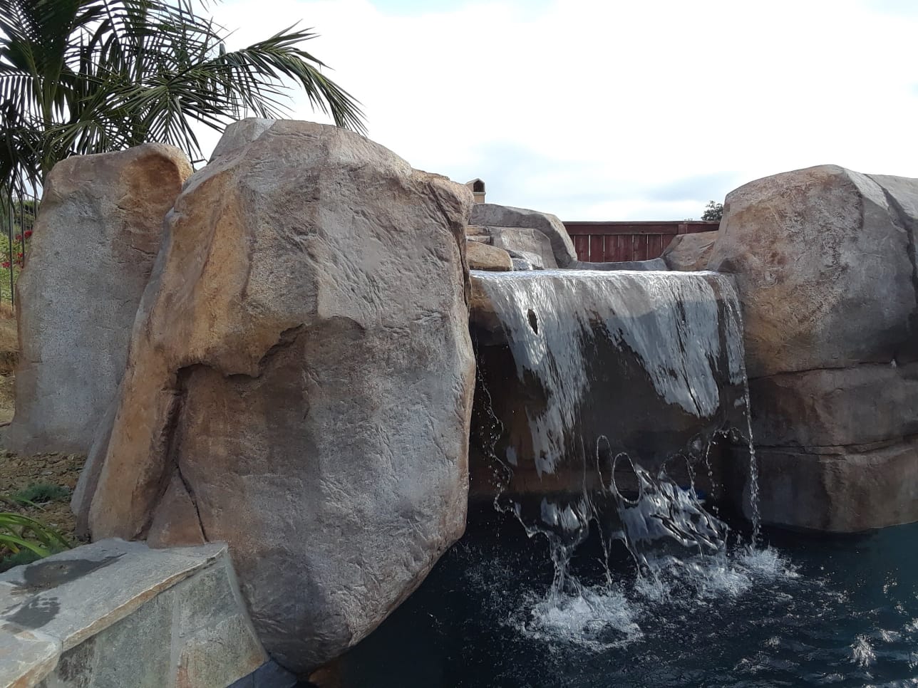 Sheet waterfall spilling between large sculpted artificial boulders into a swimming pool