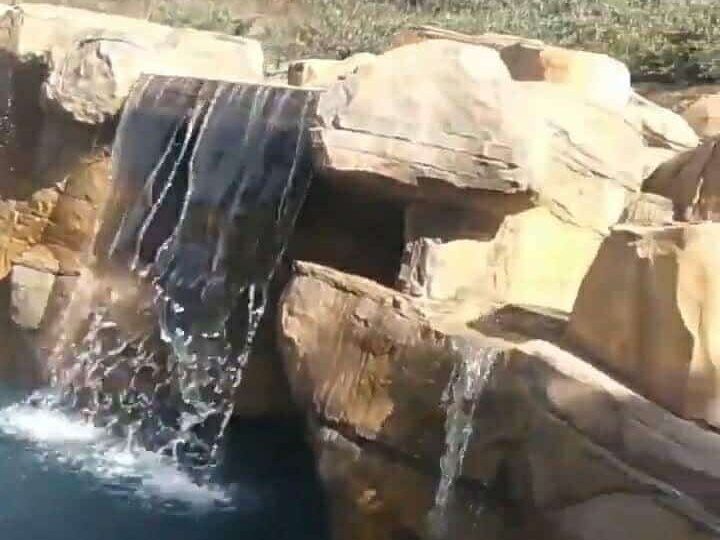 Tan sandstone-style artificial rock ledges with two waterfalls spilling into a pool